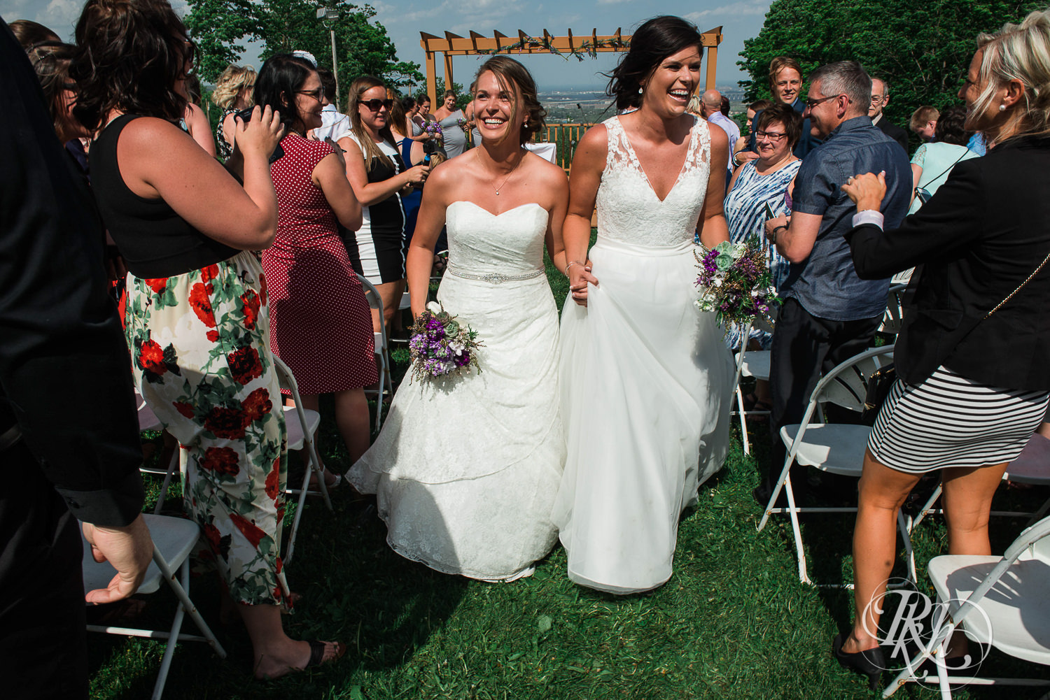 Lesbian brides laugh walking down aisle at Spirit Mountain in Duluth, Minnesota.