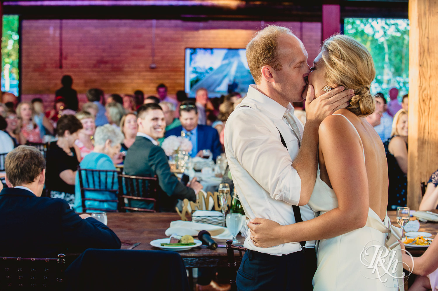 Bride and groom kiss while guests give wedding speeches at Minneapolis Event Centers in Minneapolis, Minnesota.