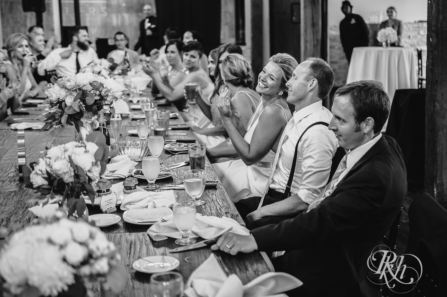 Bride and groom smile while guests give wedding speeches at Minneapolis Event Centers in Minneapolis, Minnesota.