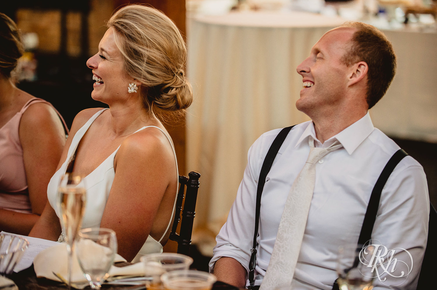 Bride and groom smile while guests give wedding speeches at Minneapolis Event Centers in Minneapolis, Minnesota.