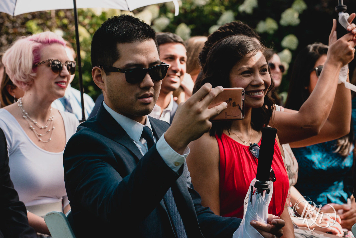 Guests take photos with iPhone during wedding ceremony at Camrose Hill Flower Farm in Stillwater, Minnesota.
