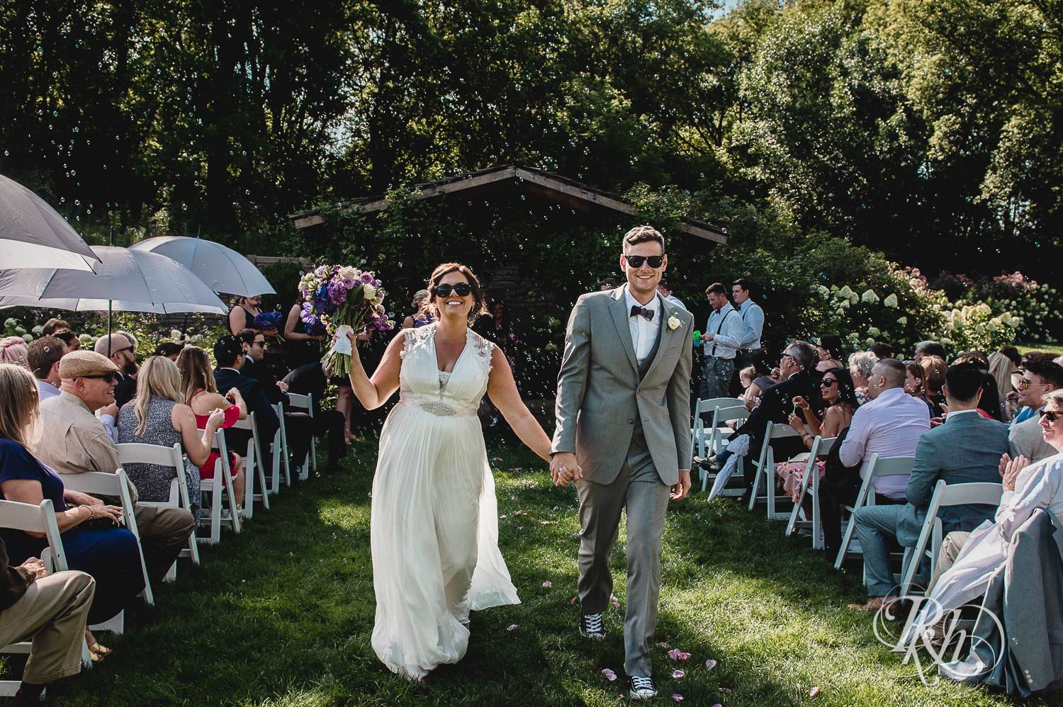 Bride and groom walk down the aisle after wedding ceremony in sunglasses at Camrose Hill Flower Farm in Stillwater, Minnesota.