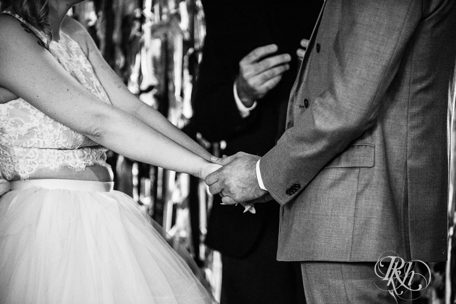 Bride and groom hold hands during wedding ceremony at Coops Event Barn in Dodge Center, Minnesota.