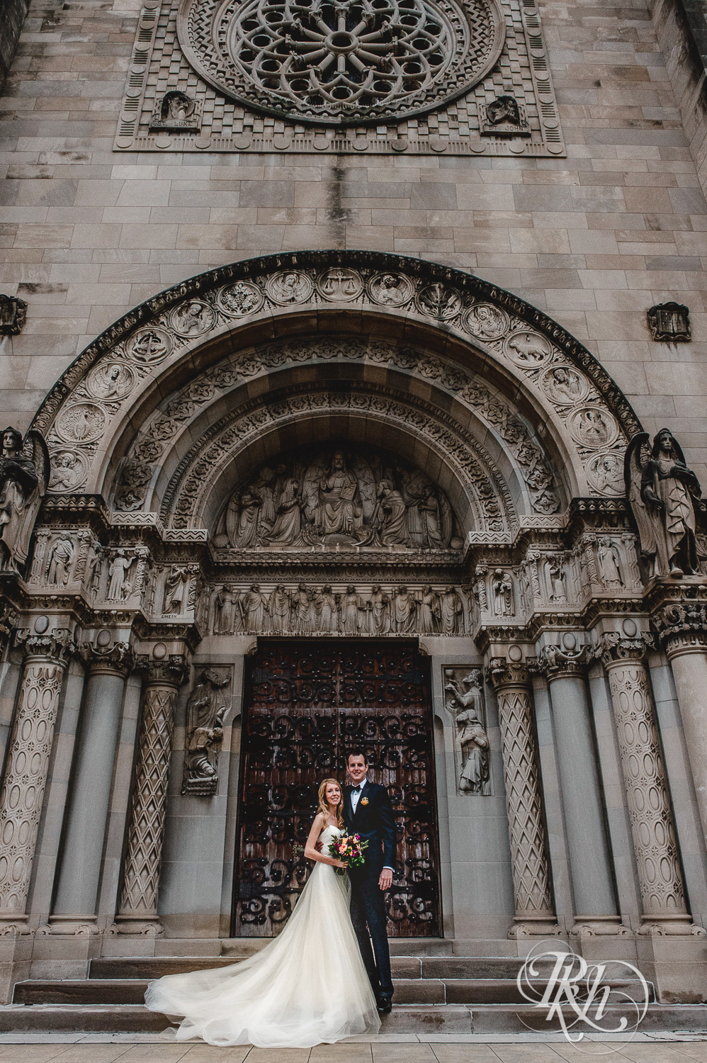 Bride and groom smile on the steps of St. Thomas Moore Catholic Church in Saint Paul, Minnesota.