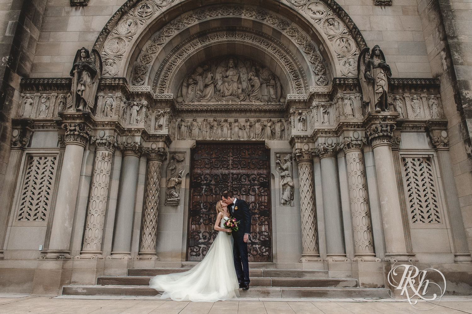 Bride and groom kiss on the steps of St. Thomas Moore Catholic Church in Saint Paul, Minnesota.