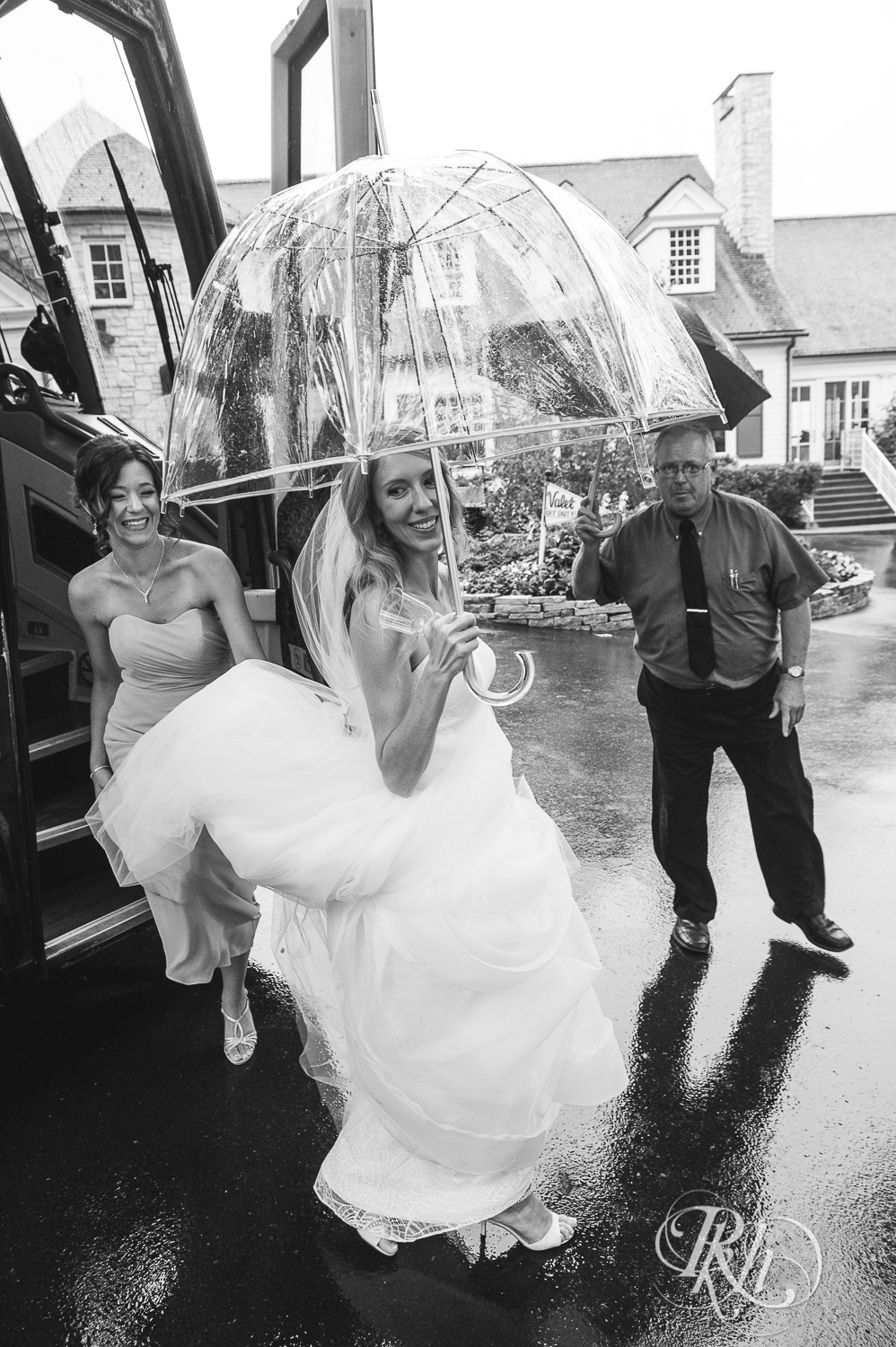 Bride walks with umbrella during rainy wedding day at White Bear Yacht Club in Dellwood, Minnesota.