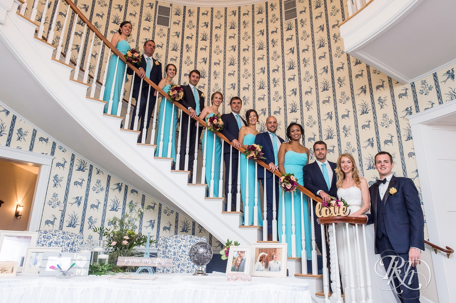 Bride and groom smile with wedding party on staircase on wedding day at White Bear Yacht Club in Dellwood, Minnesota.