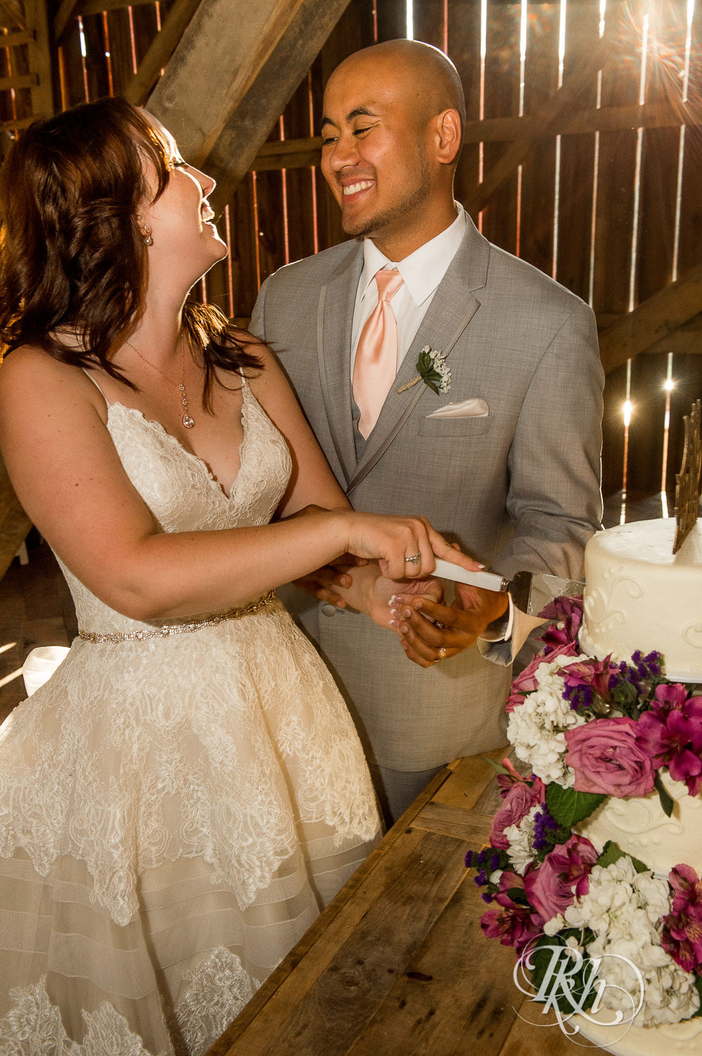 Bride and Asian groom cut cake during wedding reception at Birch Hill Barn in Glenwood City, Wisconsin.