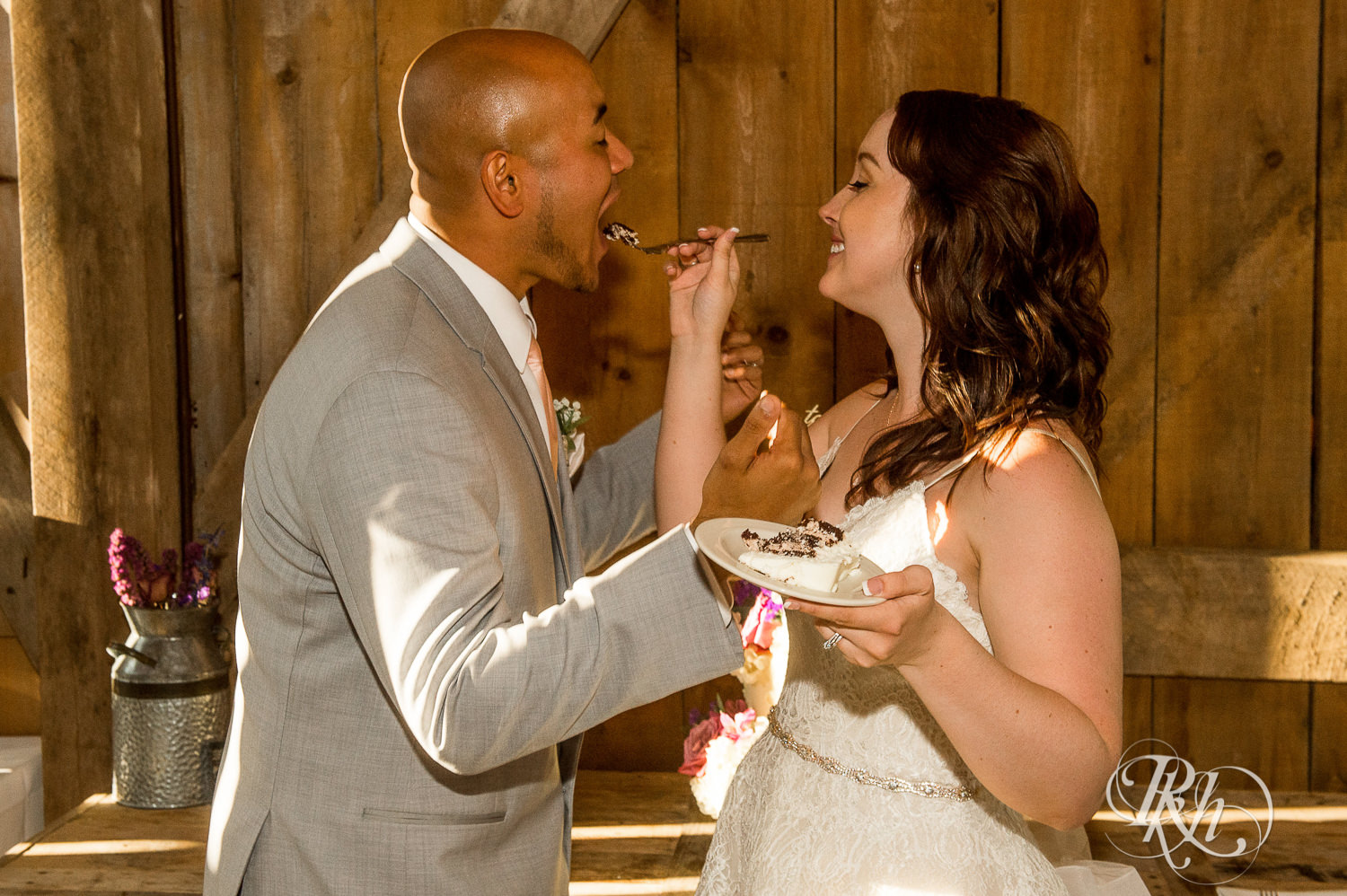 Bride and Asian groom eat cake during wedding reception at Birch Hill Barn in Glenwood City, Wisconsin.