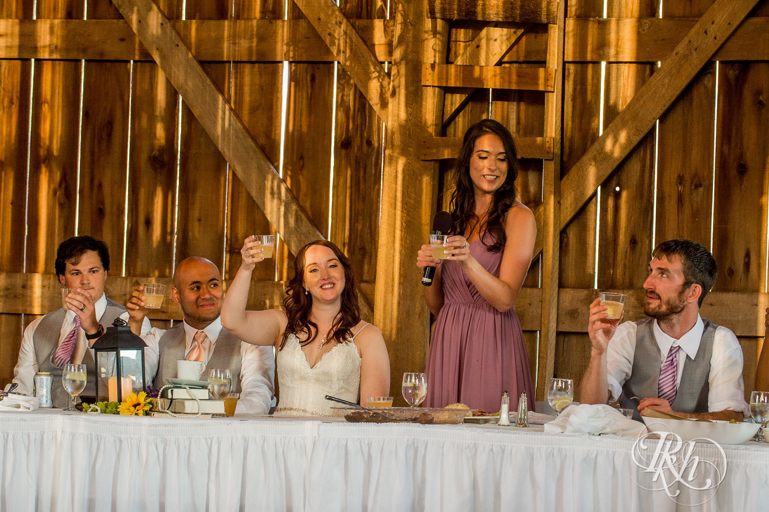 Bride and Asian groom smile during wedding reception speeches at Birch Hill Barn in Glenwood City, Wisconsin.