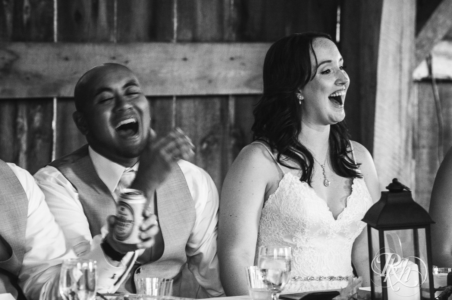 Bride and Asian groom laugh during wedding reception speeches at Birch Hill Barn in Glenwood City, Wisconsin.