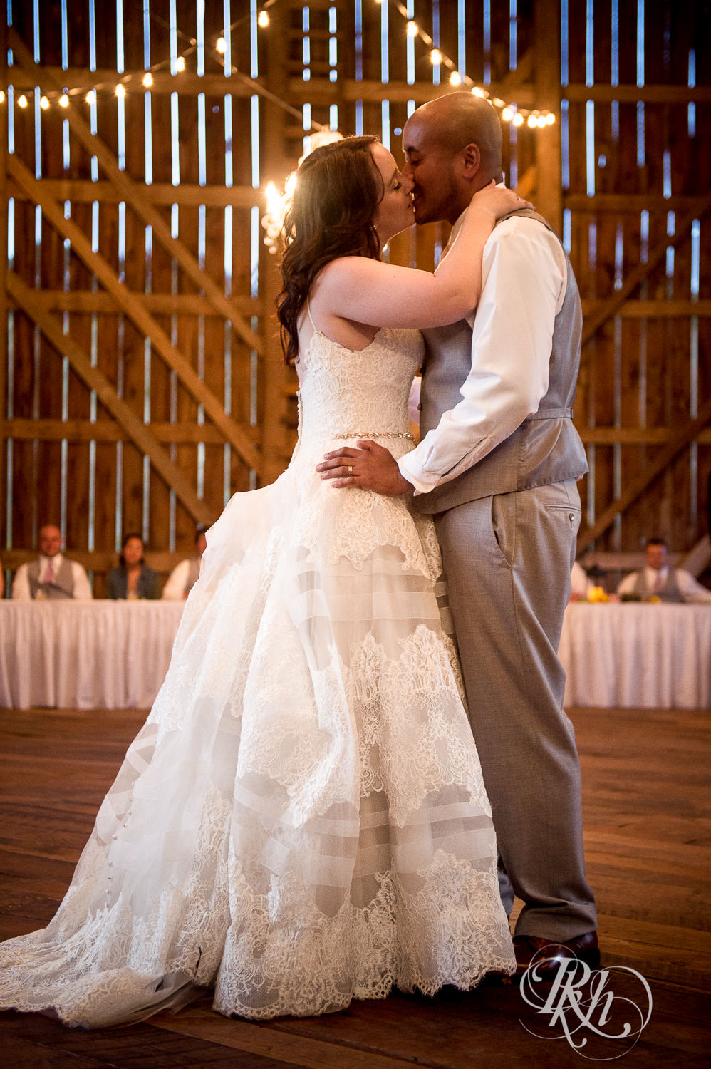 Bride and Asian groom kiss under a chandelier during wedding reception at Birch Hill Barn in Glenwood City, Wisconsin.
