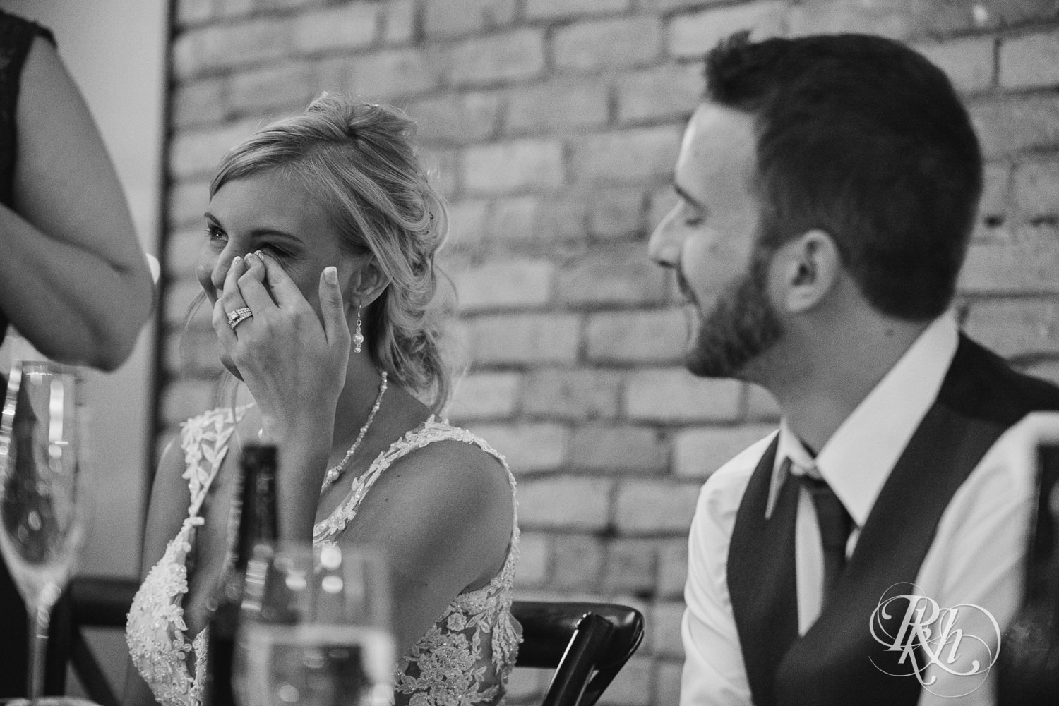 Bride and groom smile during speeches at wedding reception at the Lumber Exchange Event Center in Minneapolis, Minnesota.