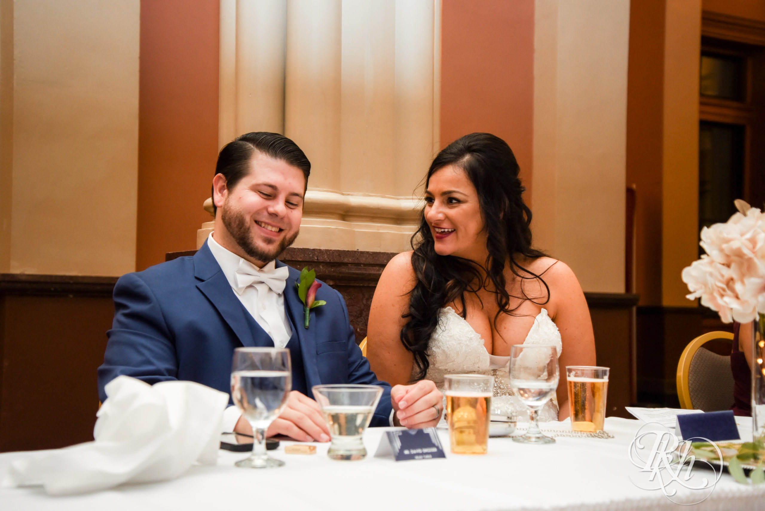 Bride and groom smile during speeches on wedding day at Landmark Center in Saint Paul, Minnesota.
