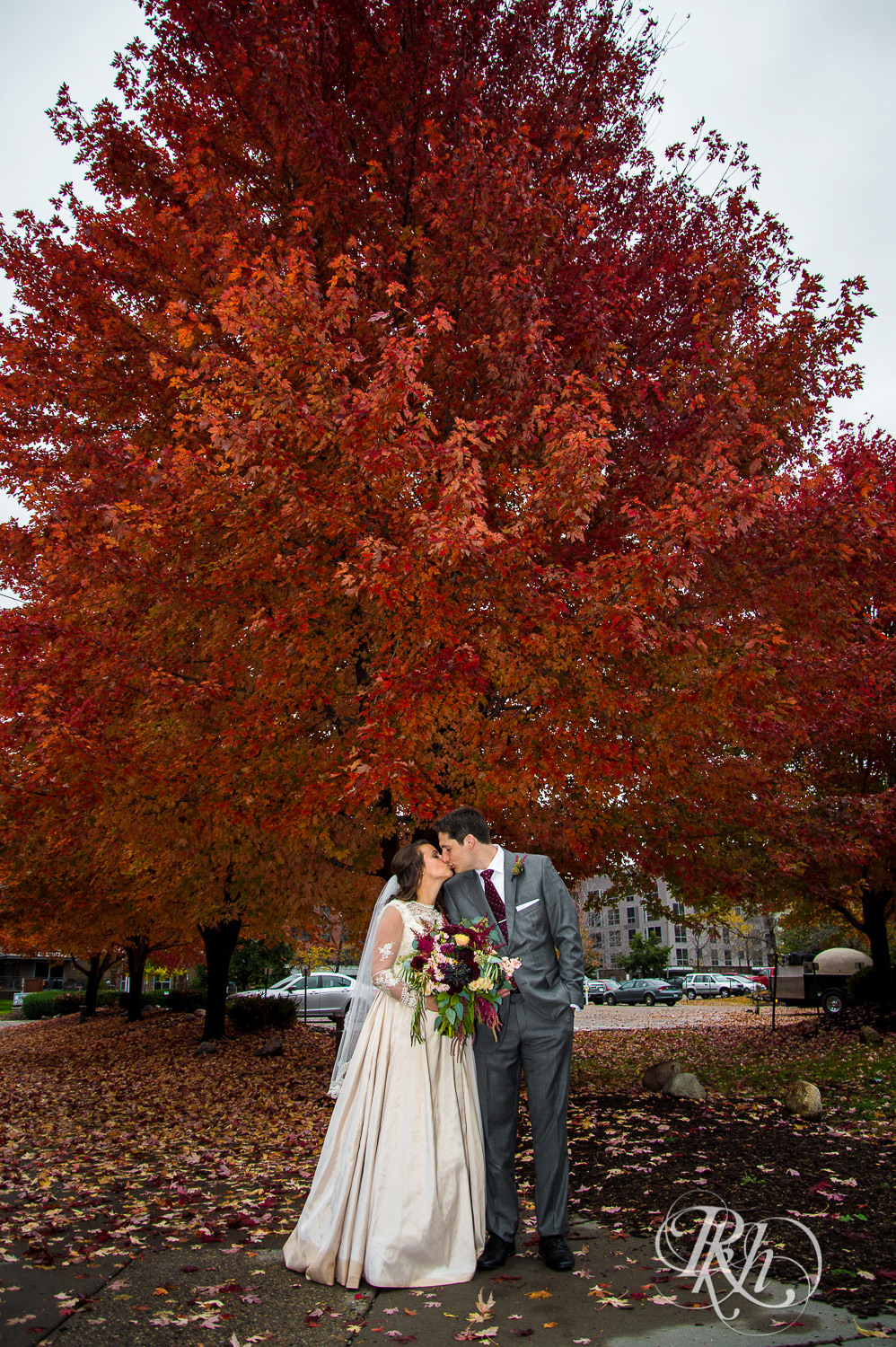 Bride and groom kiss in front of tree with red and orange leaves on a rainy wedding day in Minneapolis, Minnesota.