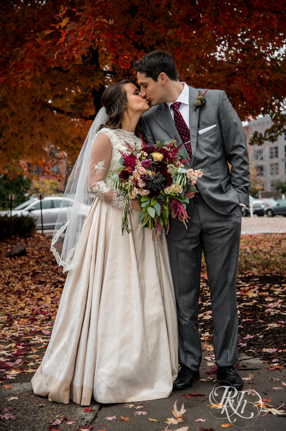 Bride and groom kiss in front of tree with red and orange leaves on a rainy wedding day in Minneapolis, Minnesota.