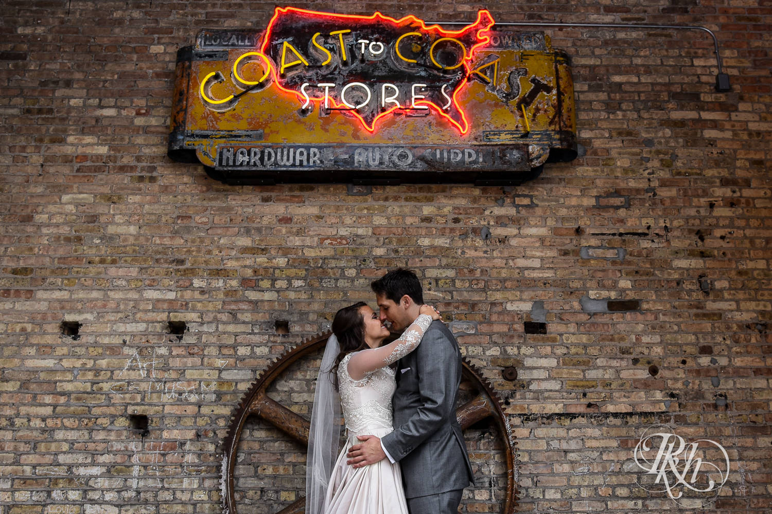 Bride and groom kiss against brick wall on a rainy wedding day in Minneapolis, Minnesota.