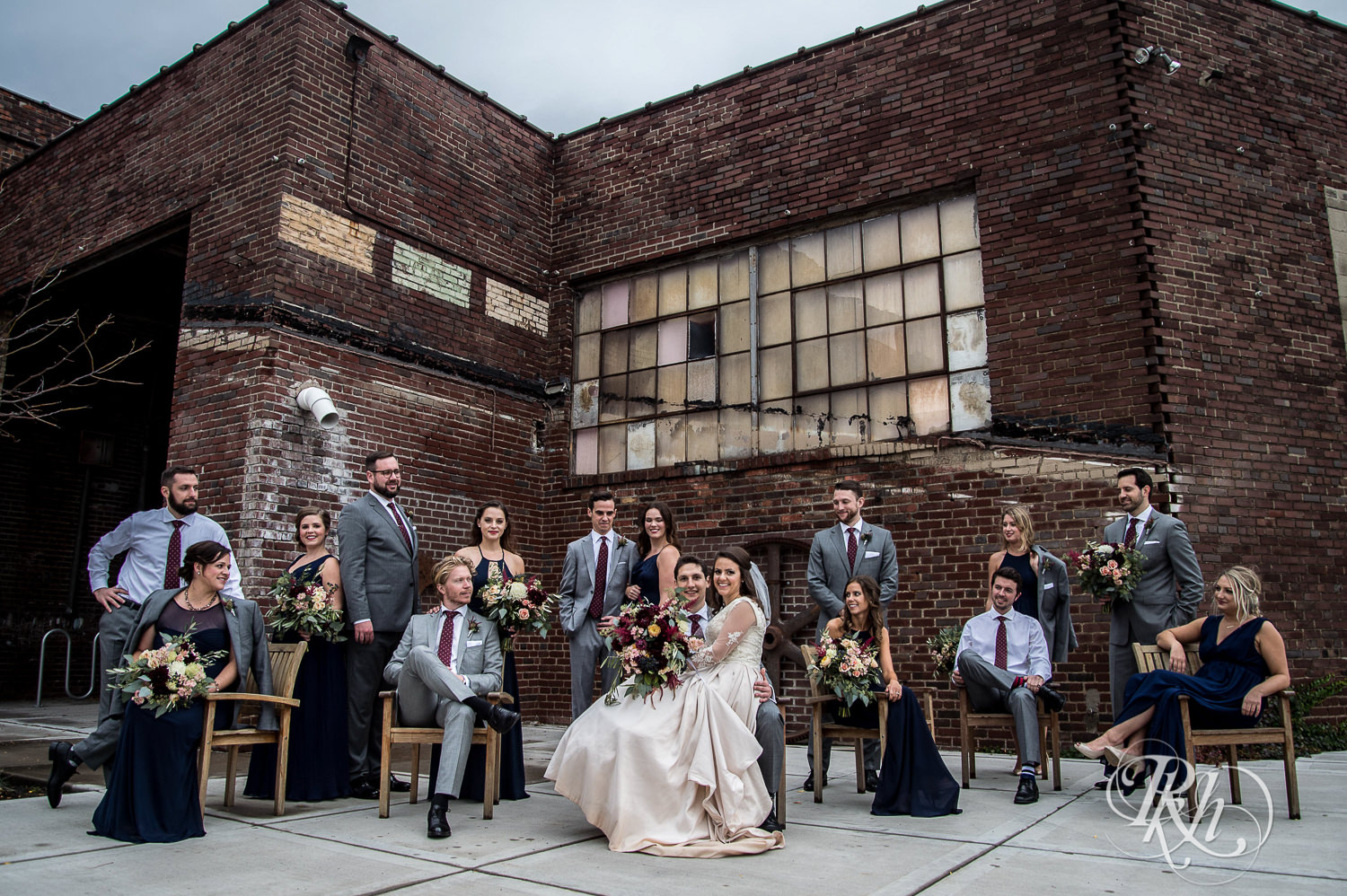 Wedding party and bride and groom smile against brick wall on a rainy wedding day in Minneapolis, Minnesota.