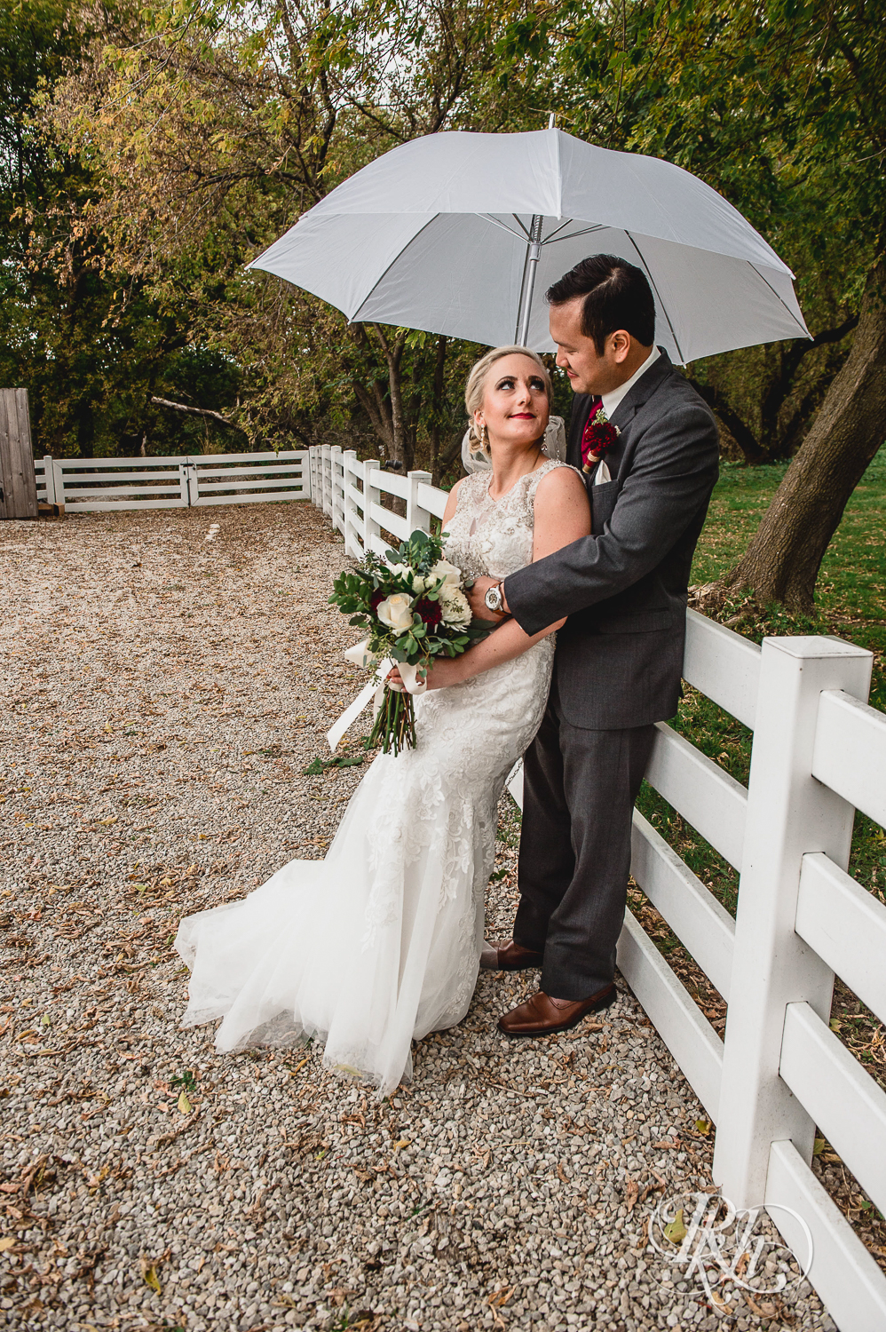 Bride and groom smile under umbrella on rainy day wedding at Green Acres Event Center in Eden Prairie, Minnesota.