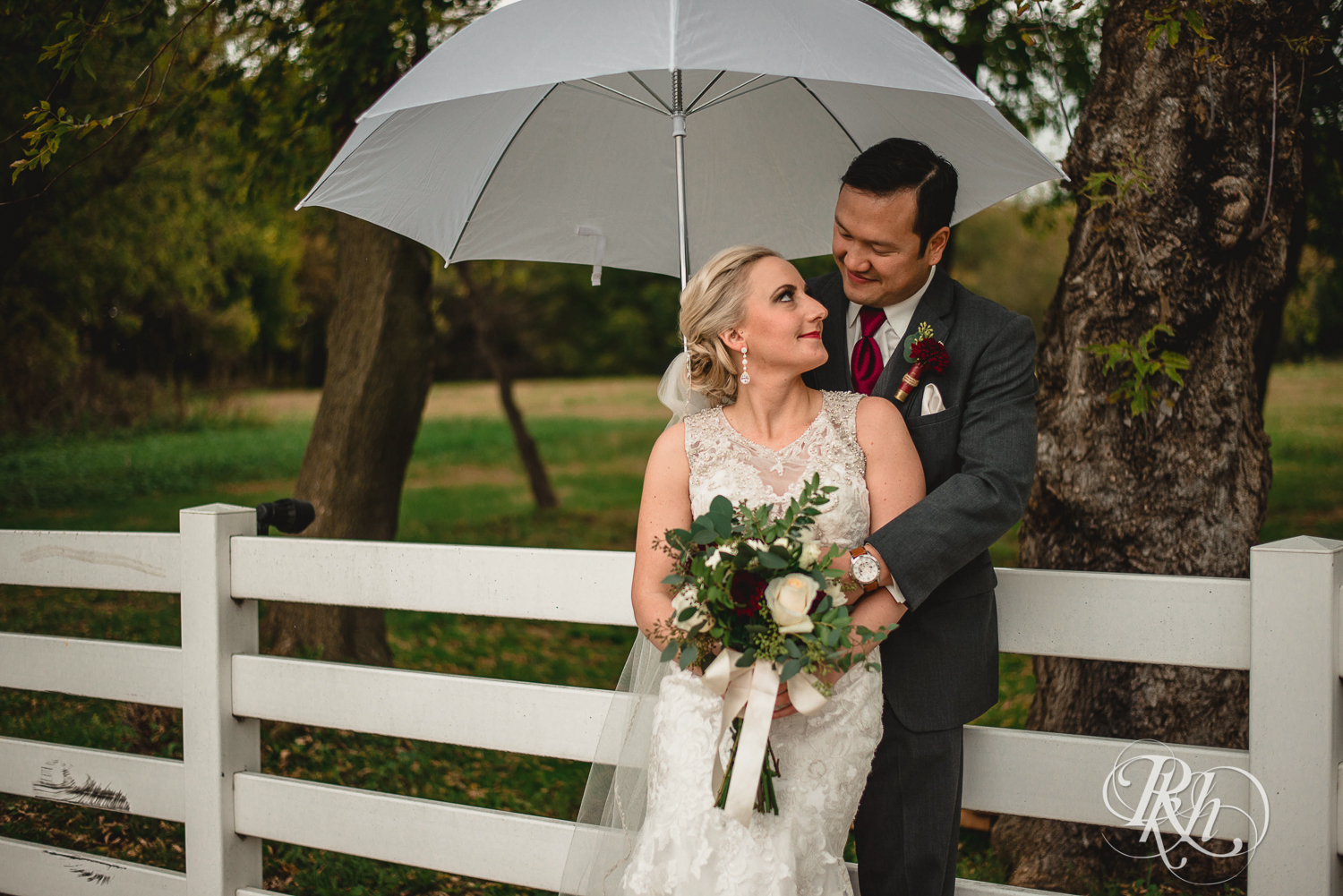 Bride and groom smile under umbrella on rainy day wedding at Green Acres Event Center in Eden Prairie, Minnesota.