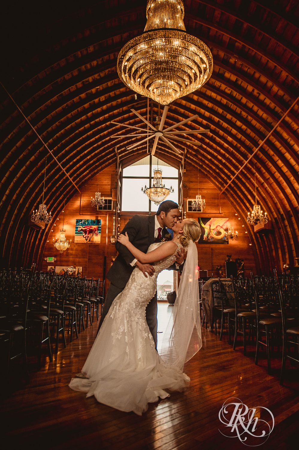 Bride and groom kiss under chandelier  at Green Acres Event Center barn wedding in Eden Prairie, Minnesota.