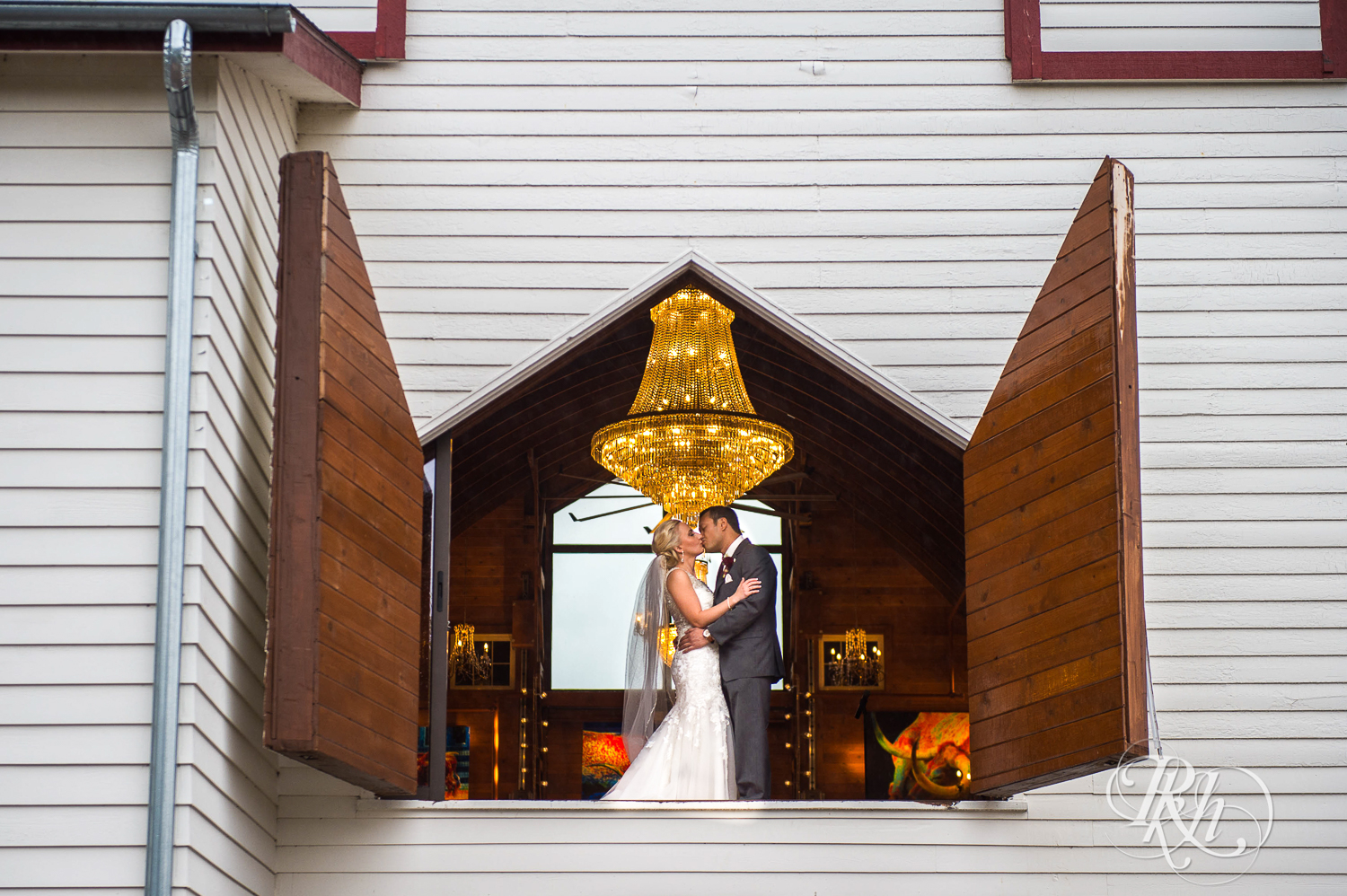 Bride and groom kiss in front of large window at Green Acres Event Center barn wedding in Eden Prairie, Minnesota.