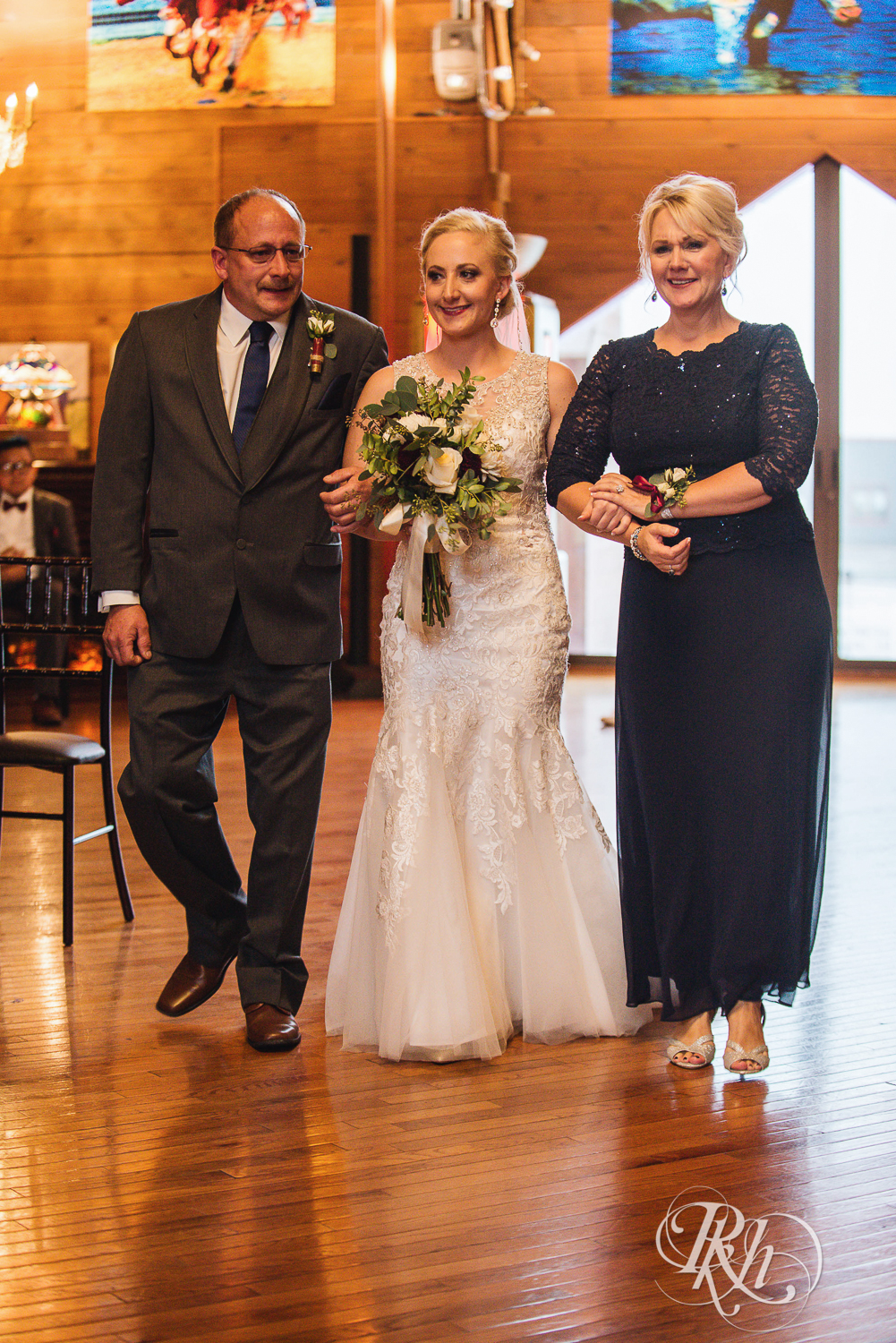 Bride walks down the aisle with parents at Green Acres Event Center barn wedding ceremony in Eden Prairie, Minnesota.