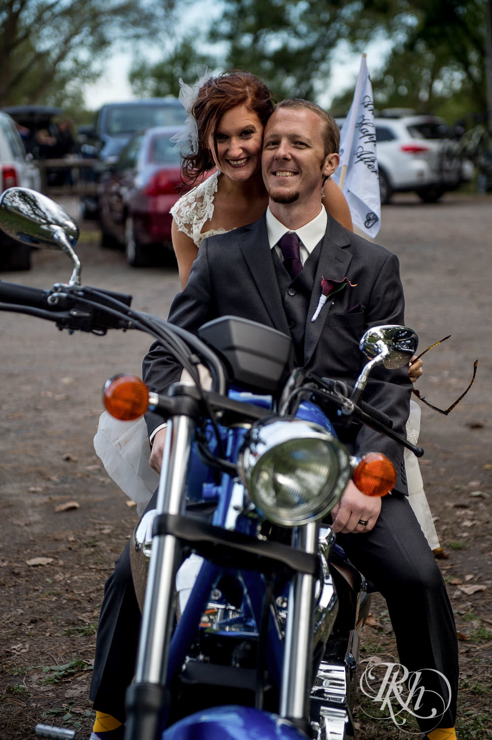 Bride and groom ride on motorcycle on wedding day at park in White Bear Lake, Minnesota.