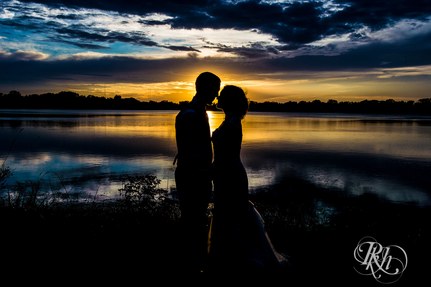 Bride and groom kiss at sunset in front of the lake in White Bear Lake, Minnesota.