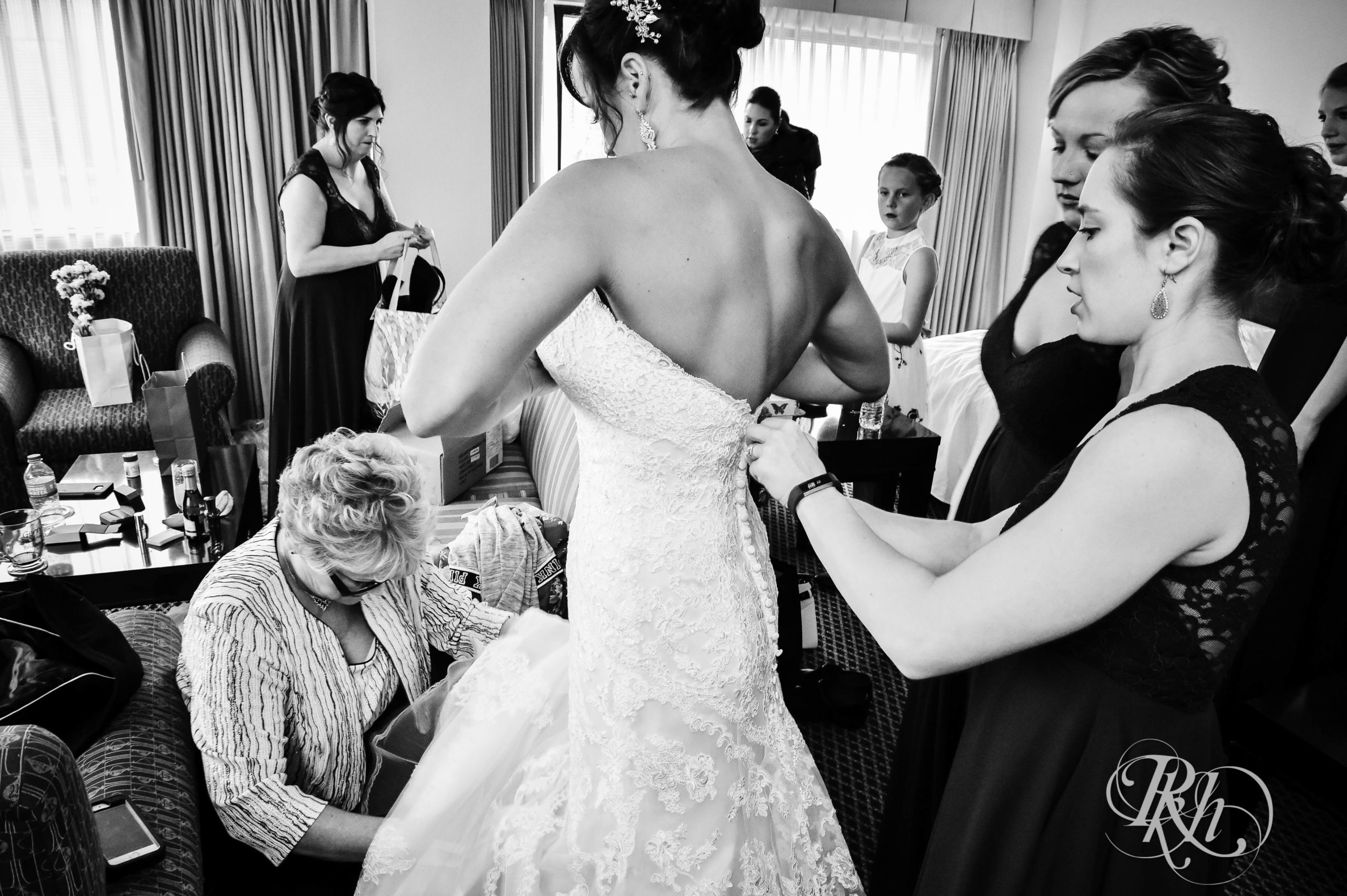 Bridesmaids and mom help bride get into wedding dress.