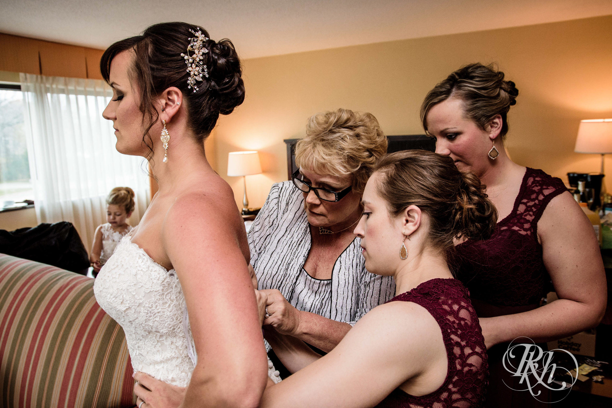 Bridesmaids and mom help bride get into wedding dress.