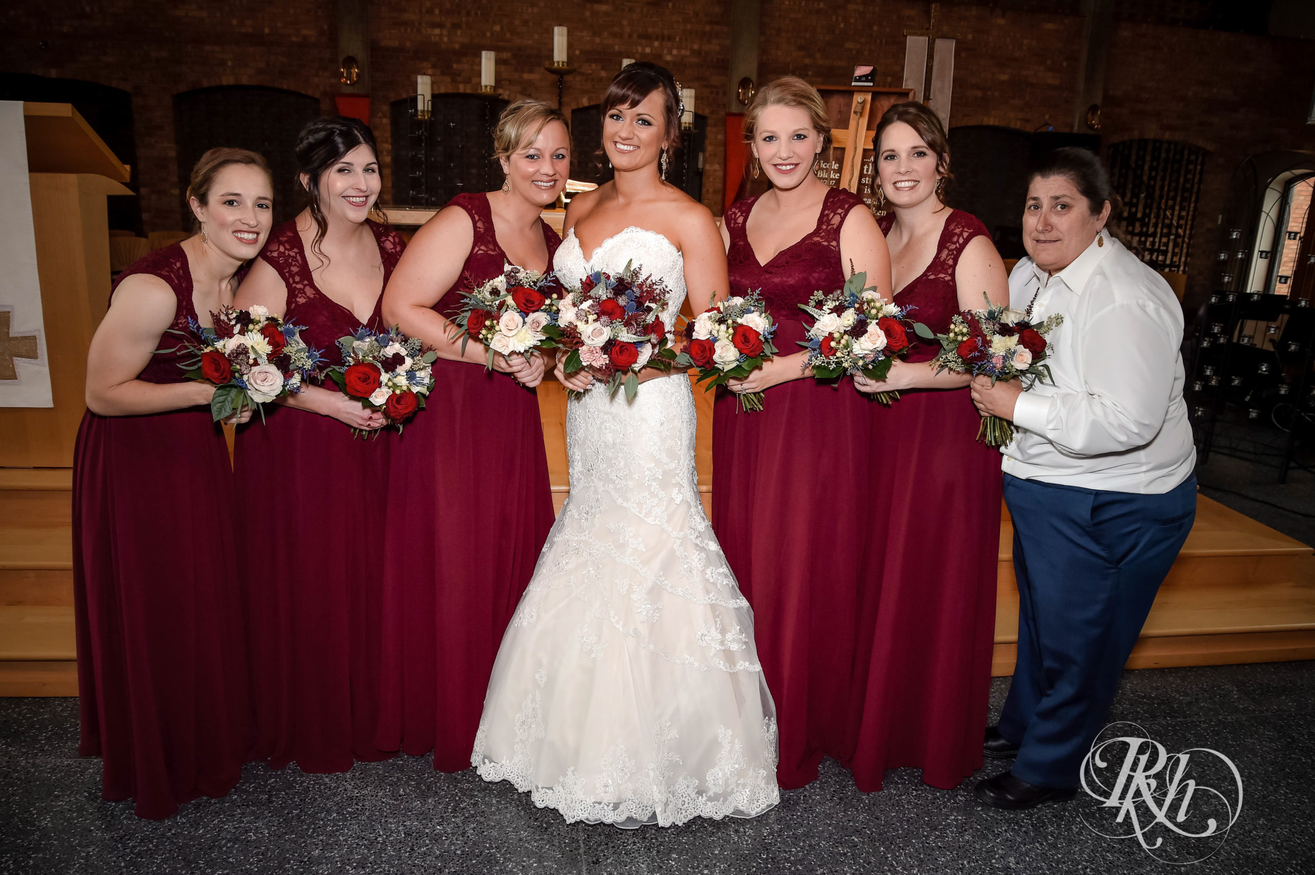 Bride smiles with wedding party in red dresses at church wedding in Minneapolis, Minnesota.