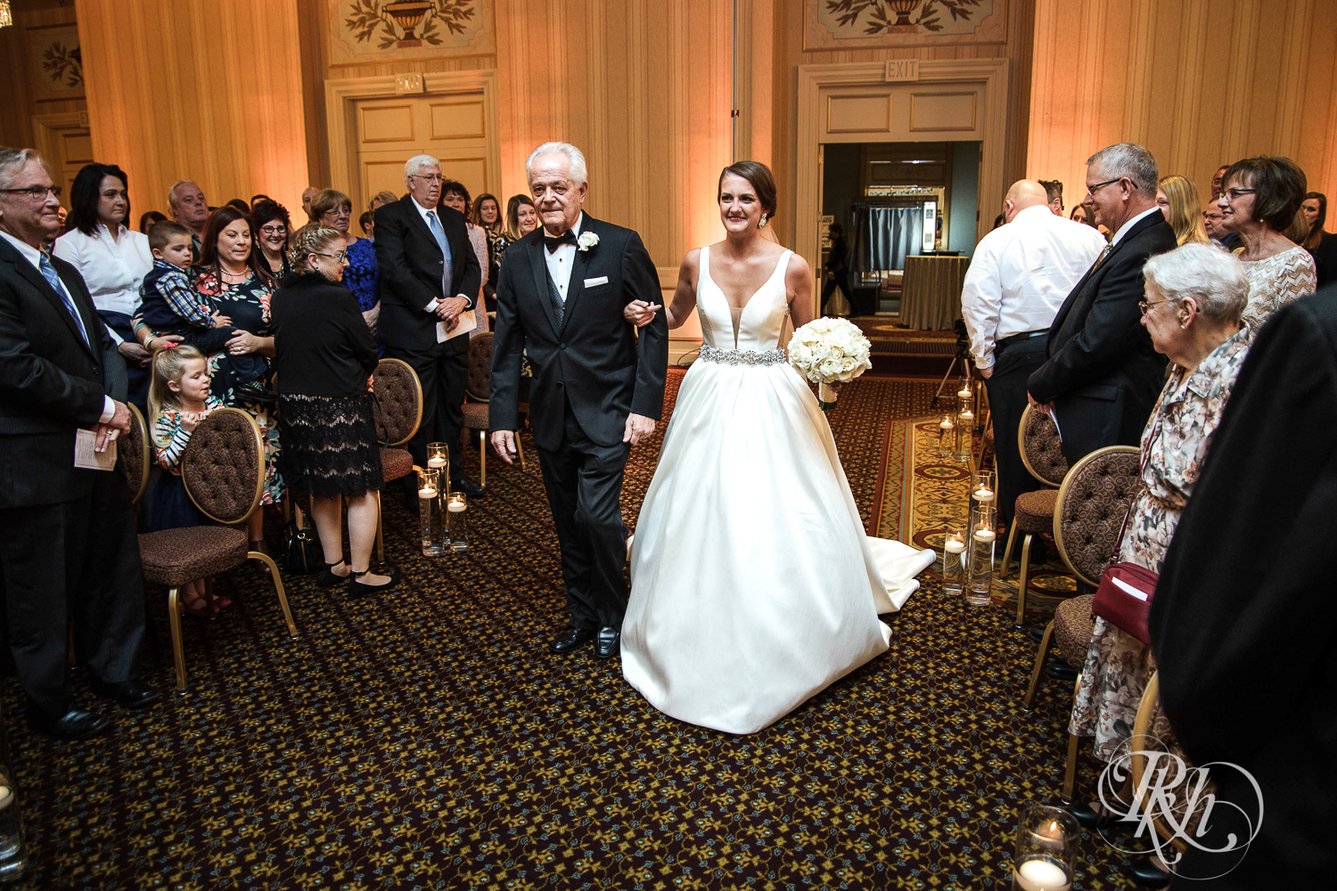 Bride walks down the aisle with dad during wedding ceremony at The Saint Paul Hotel in Saint Paul, Minnesota.