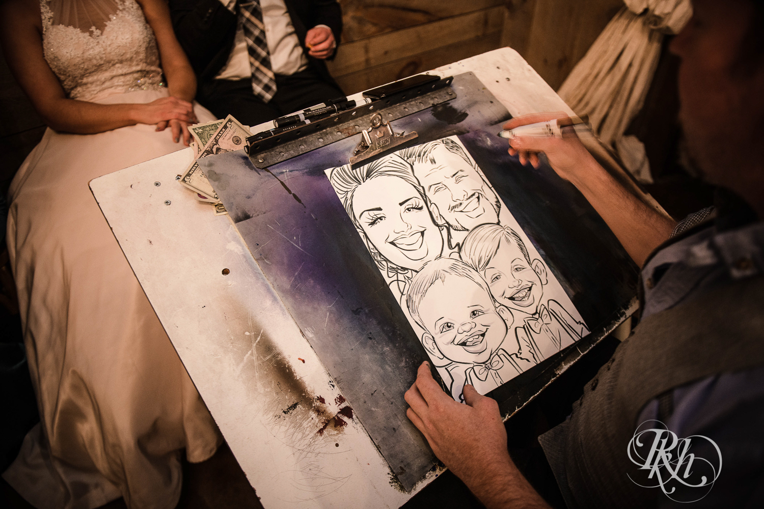 Bride and groom get caricature during wedding reception with their sons at Creekside Farm in Rush City, Minnesota.