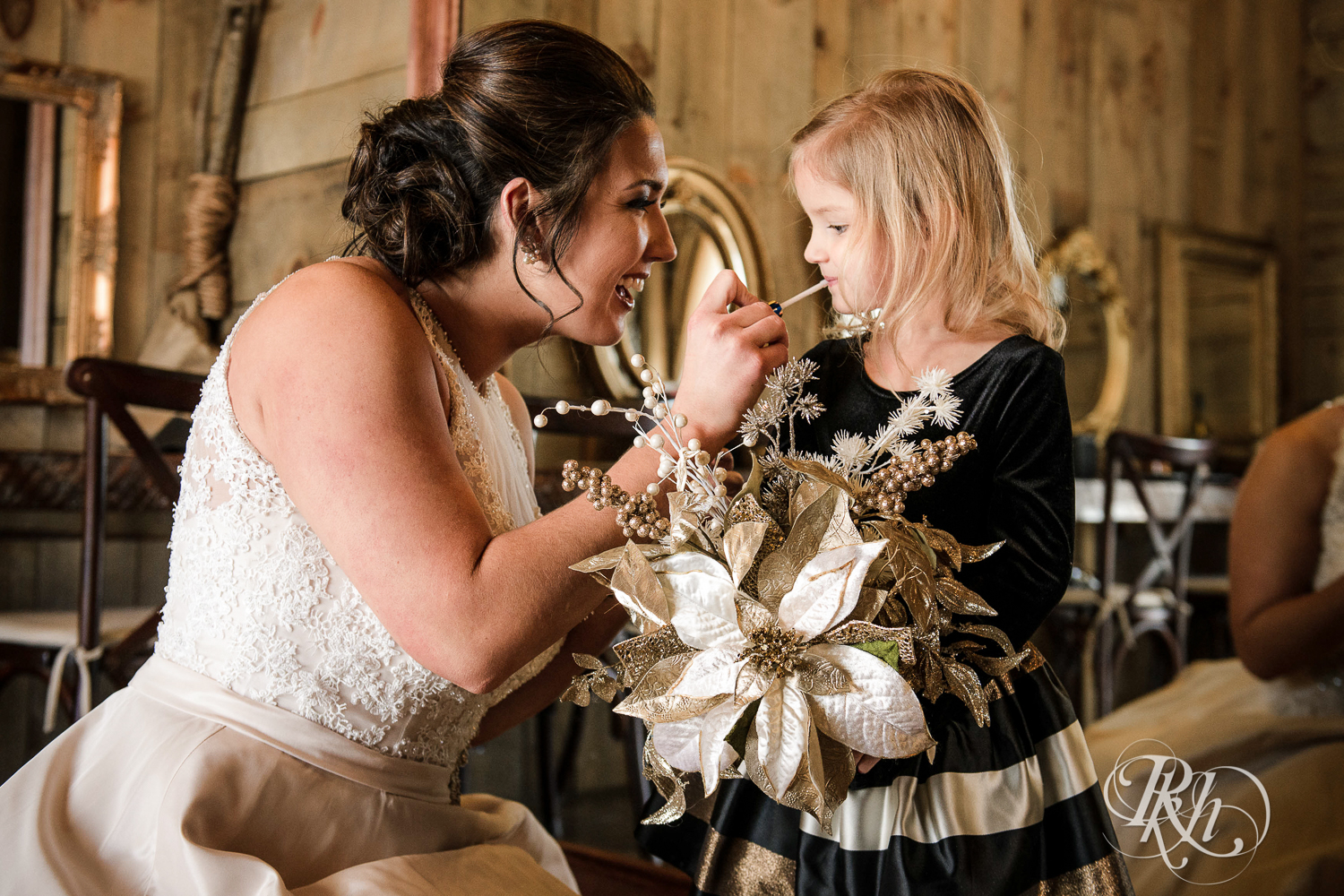 Bride puts lipstick on flower girl during winter wedding at Creekside Farm in Rush City, Minnesota.