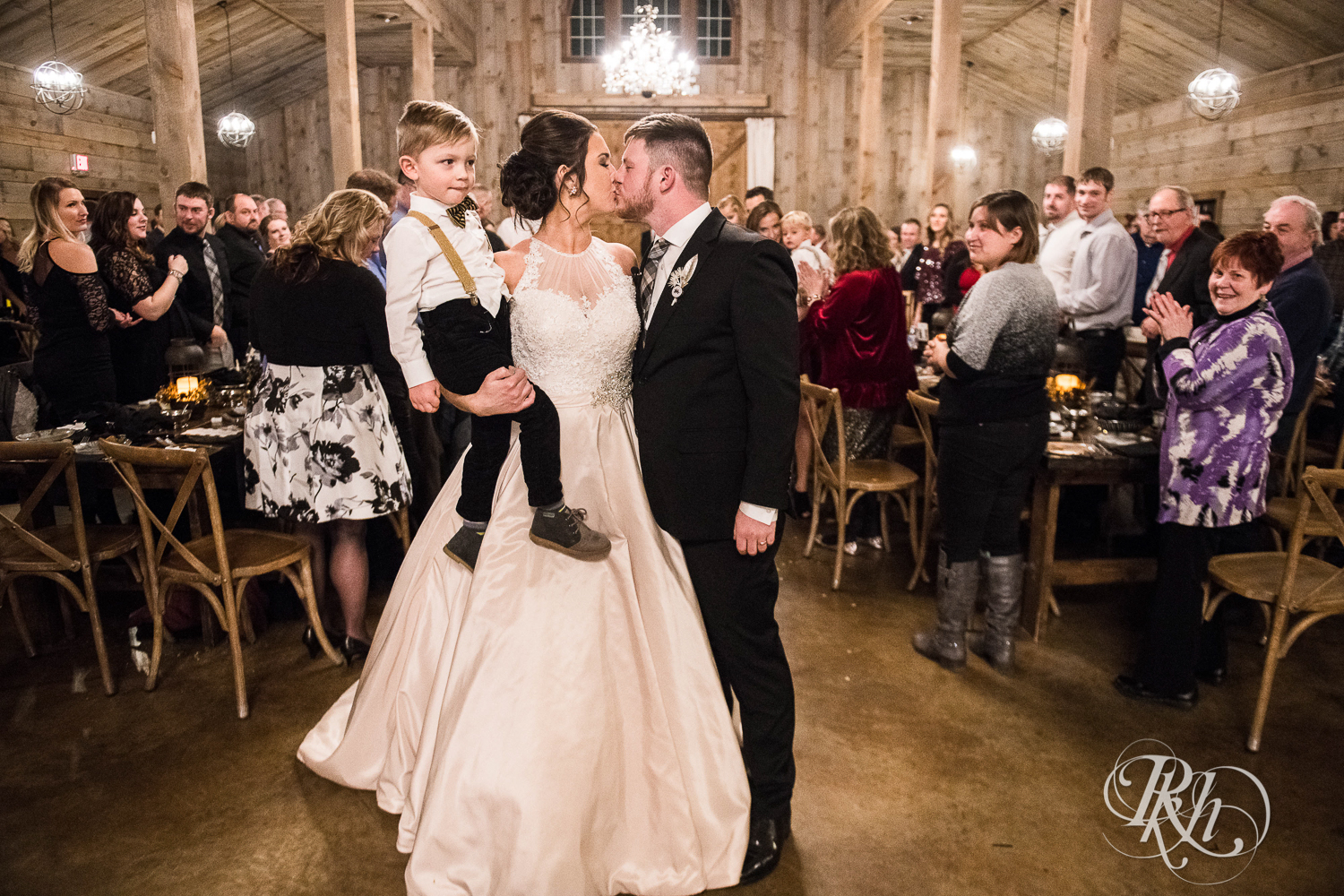 Bride and groom kiss while holding son during new year's eve wedding ceremony at Creekside Farm in Rush City, Minnesota.