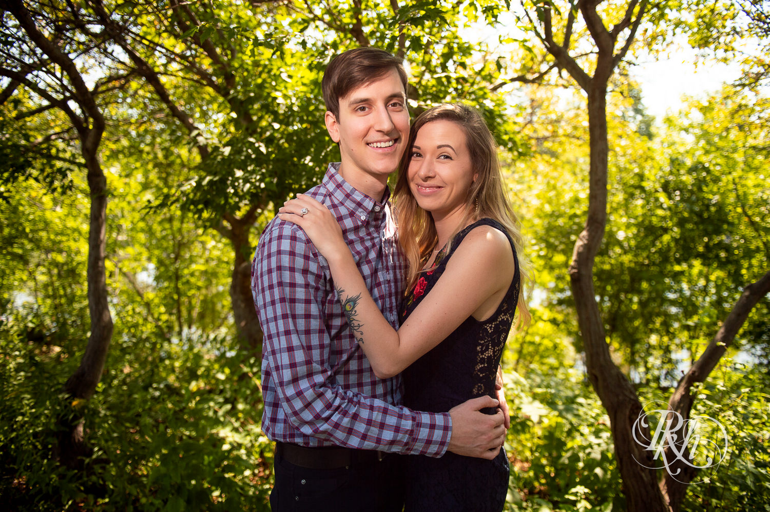 Man and woman in black lace dress smile during summer Boom Island Park engagement photos in Minneapolis, Minnesota.