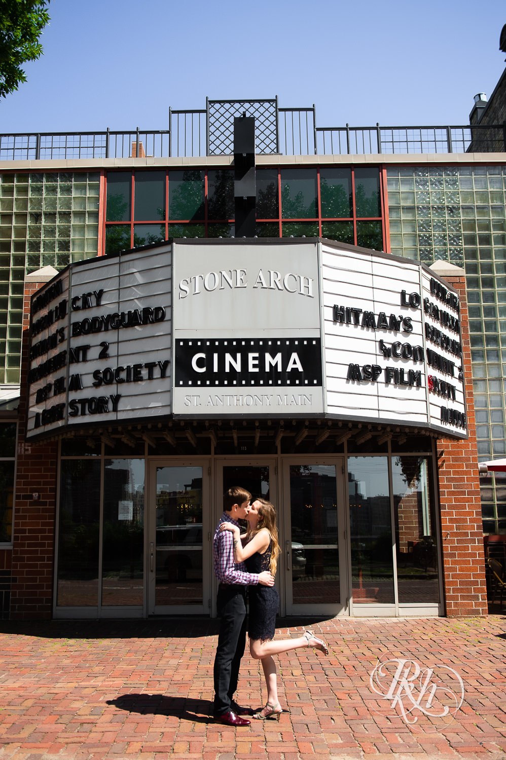 Man and woman in black lace dress kiss in front of Stone Arch Cinema in Saint Anthony Main in Minneapolis, Minnesota.