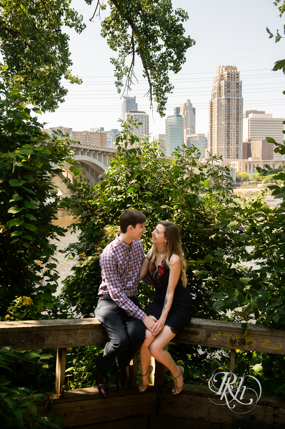 Man and woman in black lace dress smile in Saint Anthony Main in Minneapolis, Minnesota in front of the city skyline.