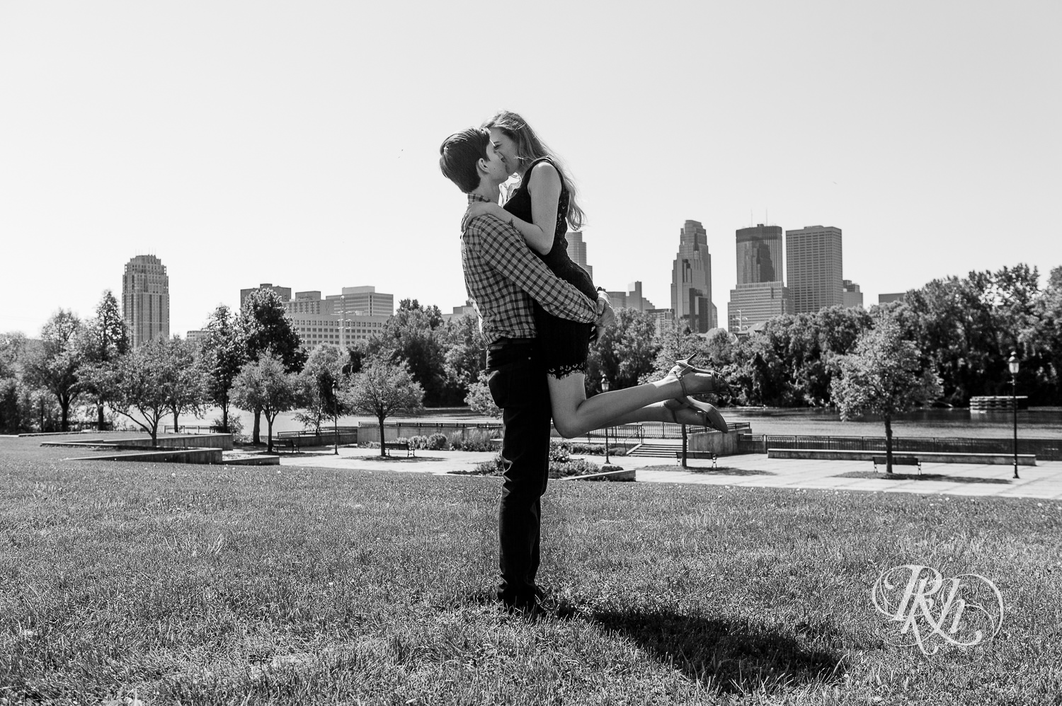 Man and woman in black lace dress kiss in front of Minneapolis skyline at Boom Island Park.