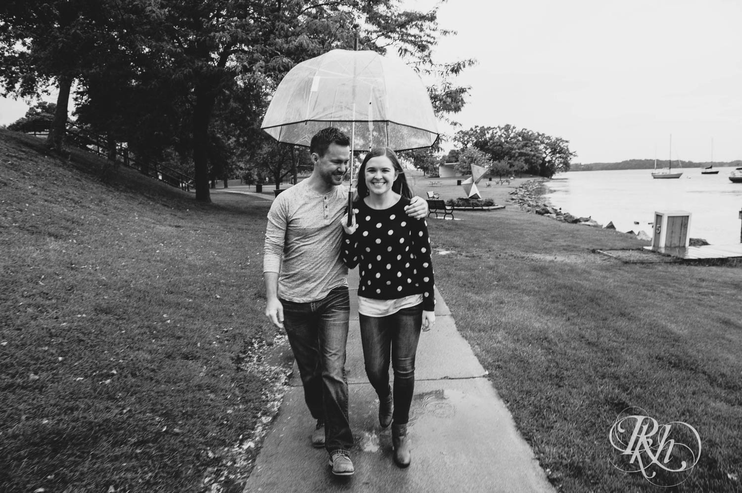 Man and woman laugh under umbrella during rainy day engagement photos in Excelsior, Minnesota.