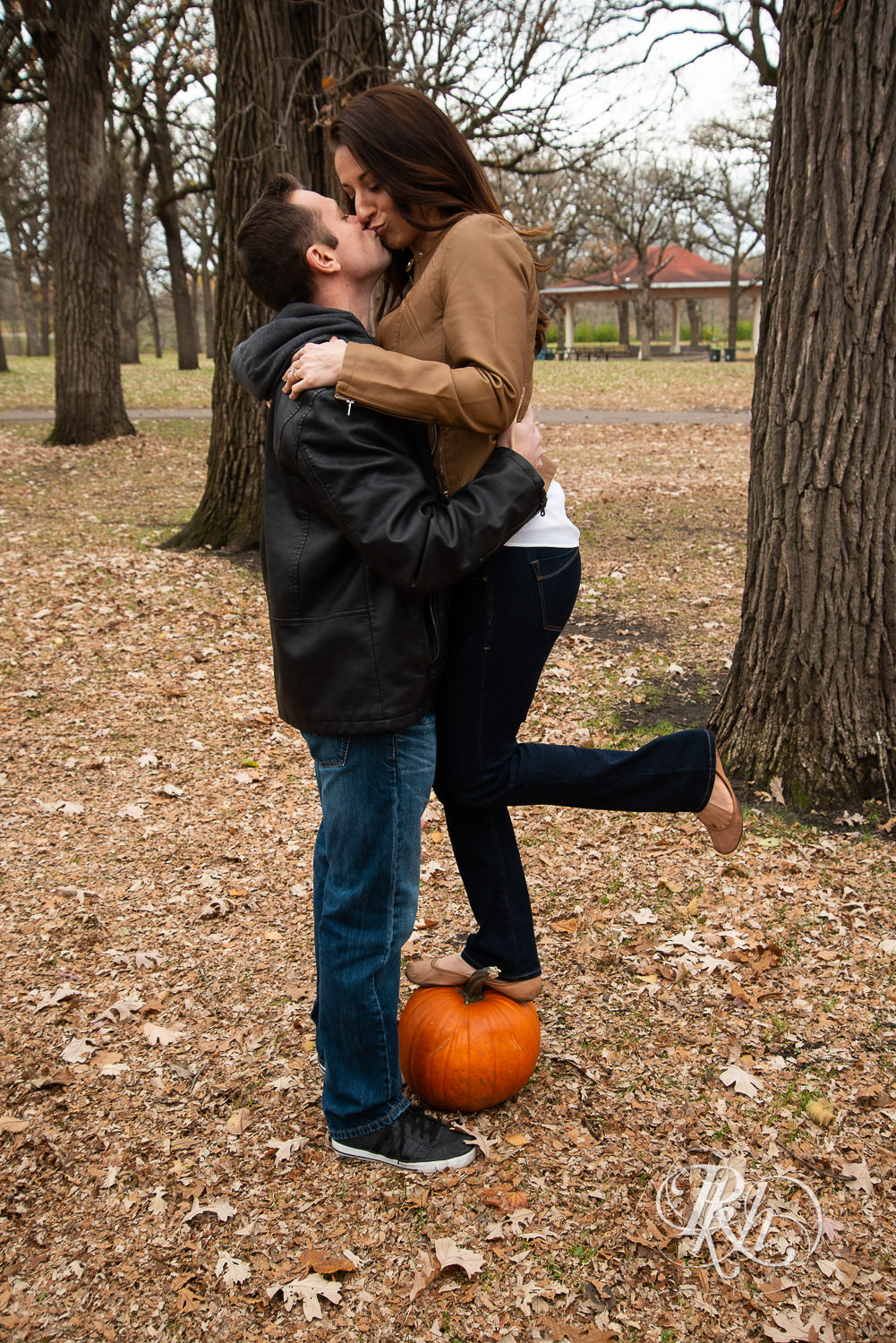 Man kissing a woman standing on a pumpkin during Minnehaha Falls engagement photos in Minneapolis, Minnesota.