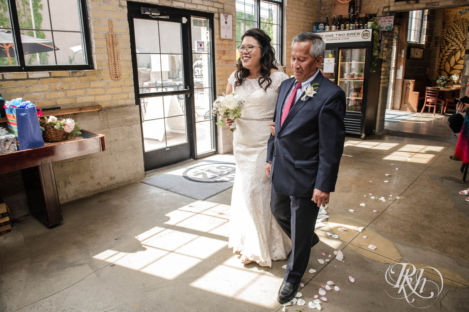 Asian bride walks down the aisle during wedding ceremony at 612 Brew in Minneapolis, Minnesota.