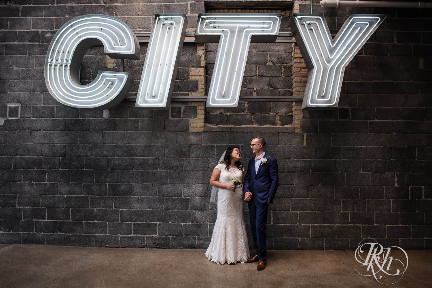 Asian bride and groom smile under city sign at 612 Brew in Minneapolis, Minnesota.