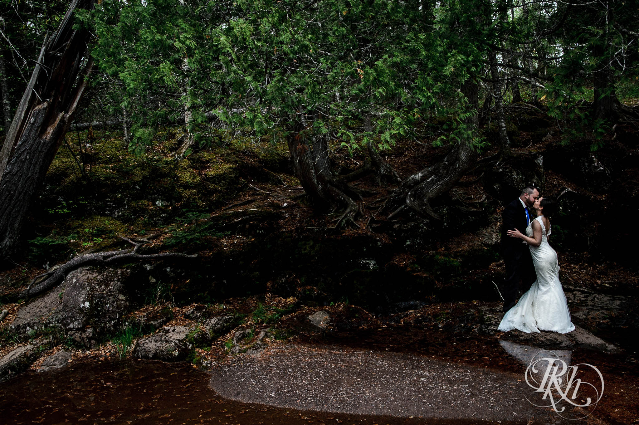 Bride and groom kiss on cliff at the bottom of a waterfall in North Shore in Minnesota.