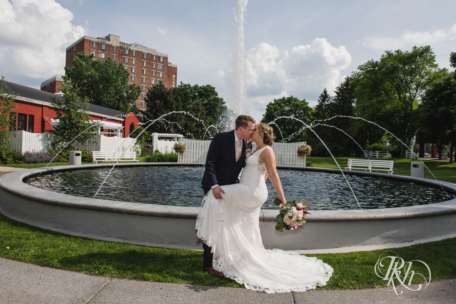 Bride and groom kiss in front of fountain on wedding day at Earle Brown Heritage Center in Brooklyn Center, Minnesota.