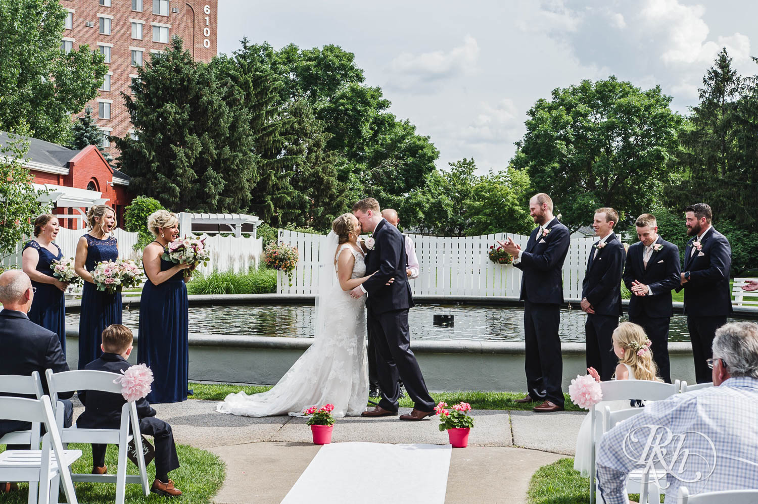 Bride and groom kiss during outdoor wedding ceremony at Earle Brown Heritage Center in Brooklyn Center, Minnesota.