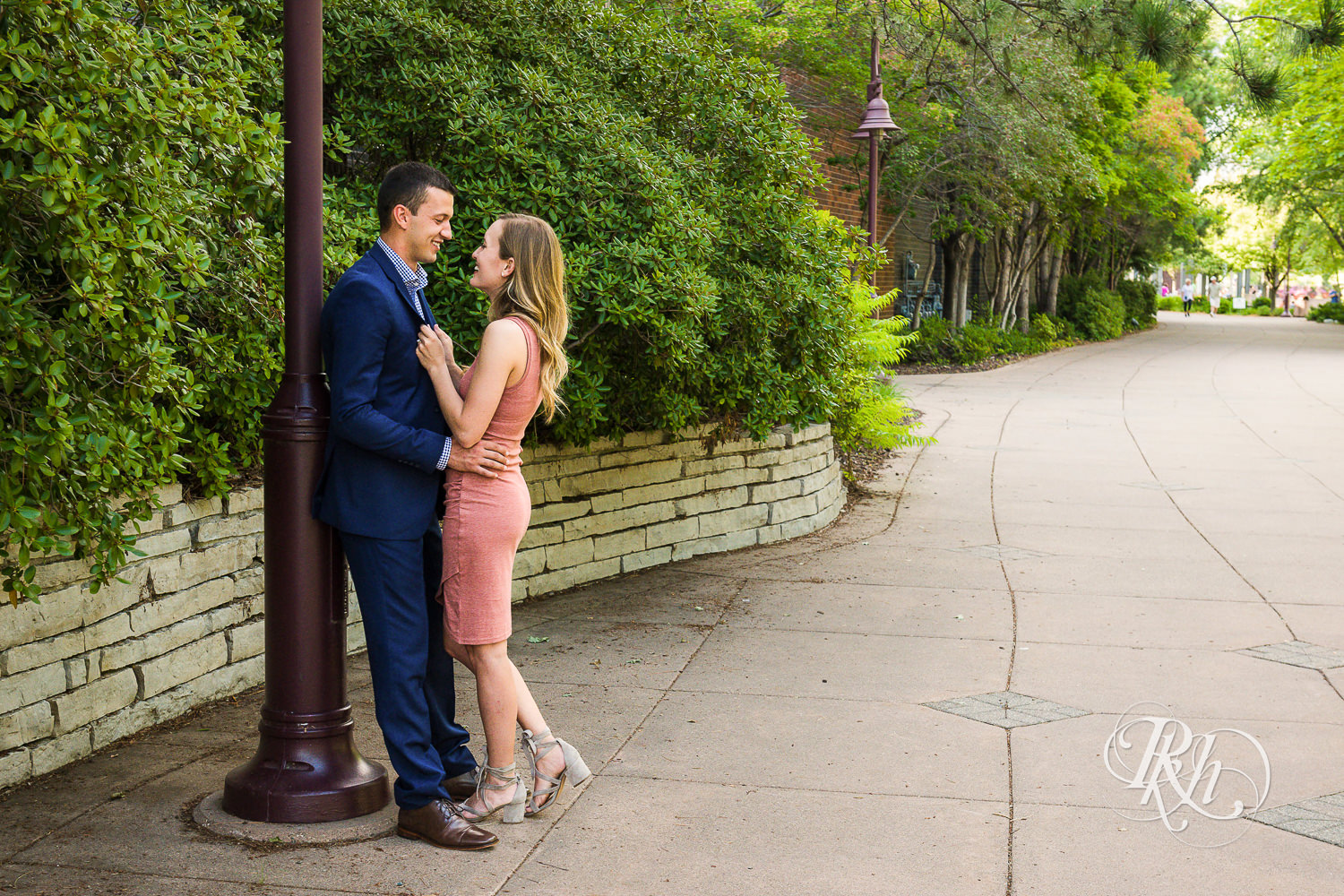 Man in blue suit and woman in pink dress smile during Centennial Lakes Park engagement photography in Edina, Minnesota.
