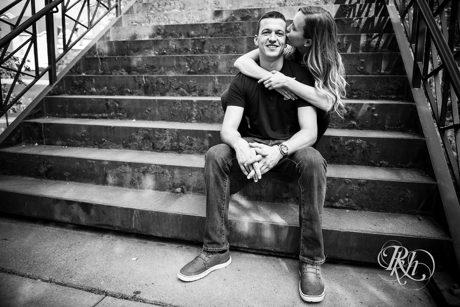 Man and woman in T-shirts and jeans kiss on stairs in Centennial Lakes Park in Edina, Minnesota.