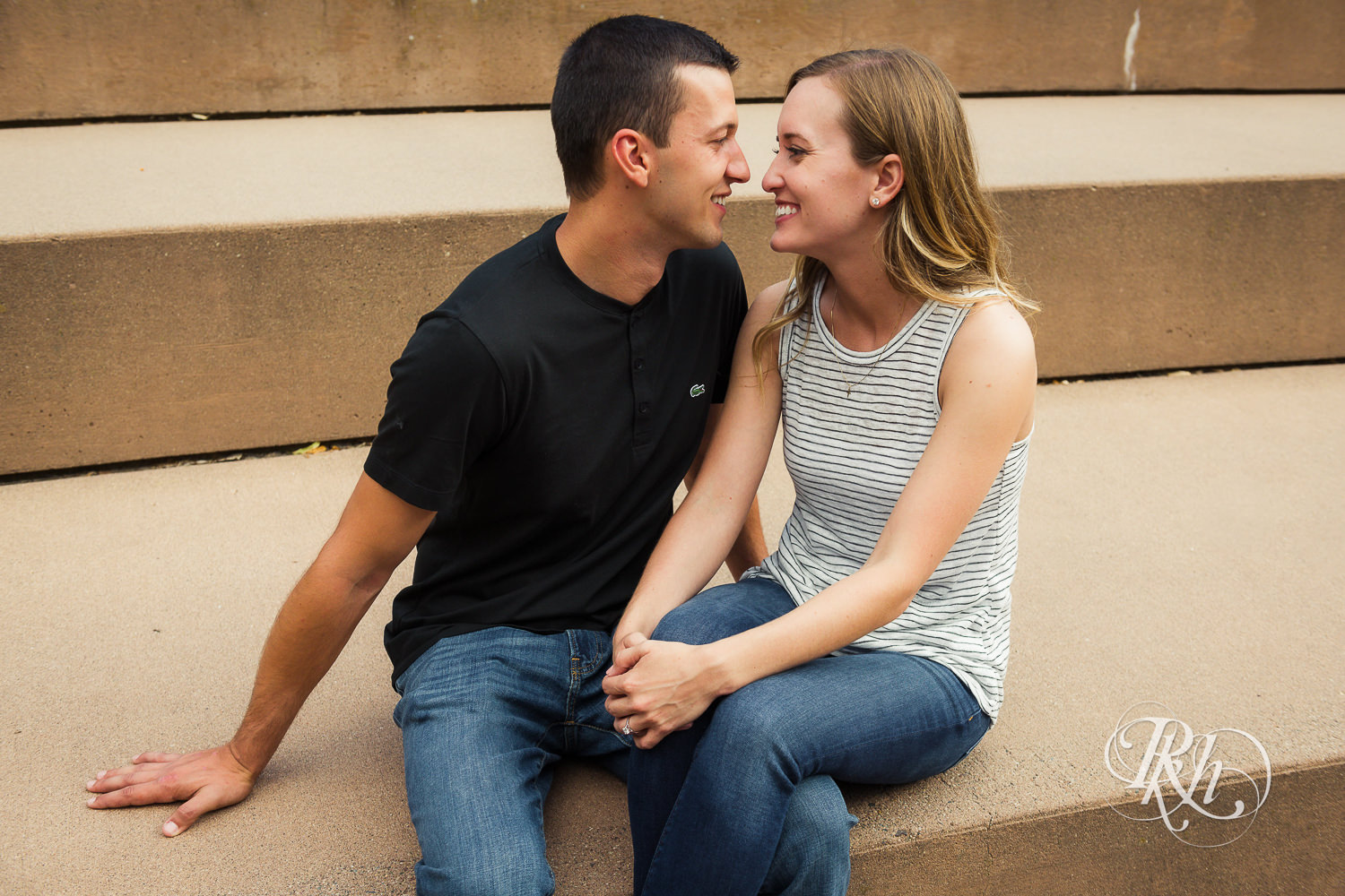 Man and woman in T-shirts and jeans smile on stairs in Centennial Lakes Park in Edina, Minnesota.